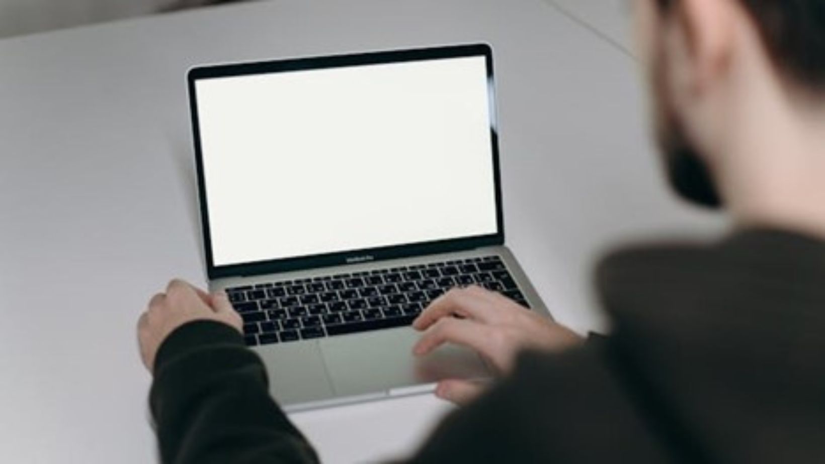 Man in a black shirt typing on a laptop.