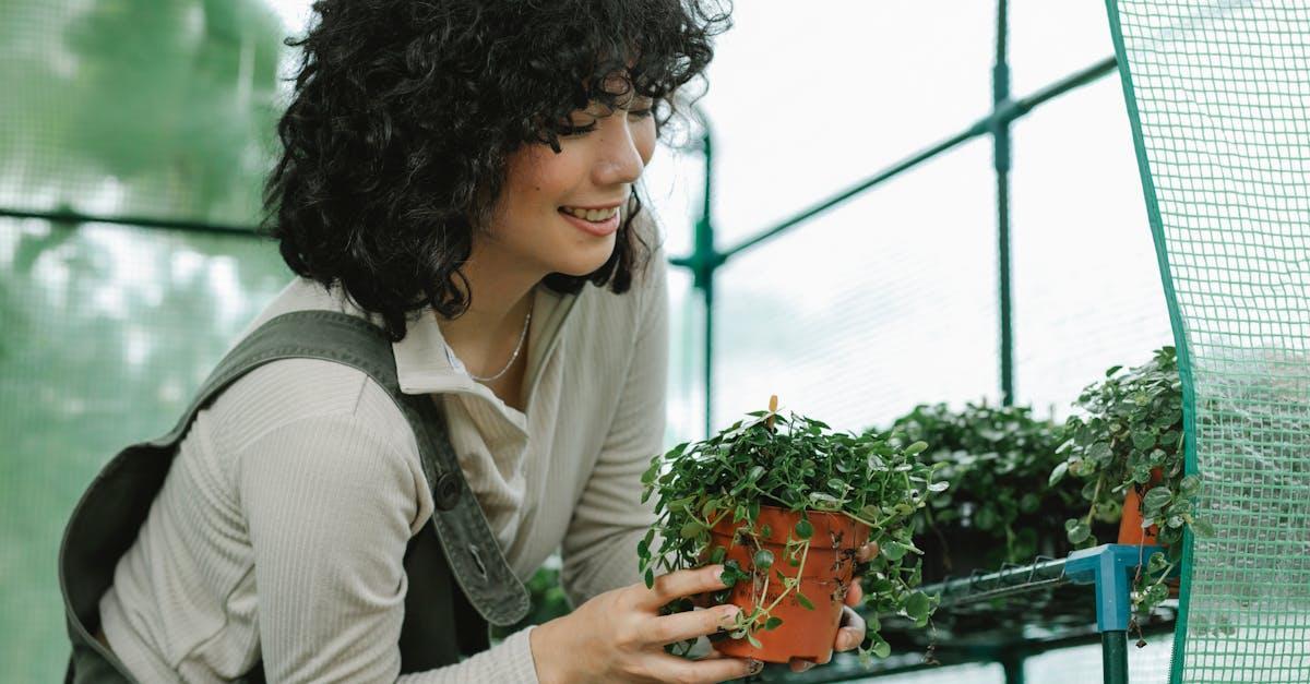 Smiling woman nurturing potted plants in a greenhouse, promoting growth.